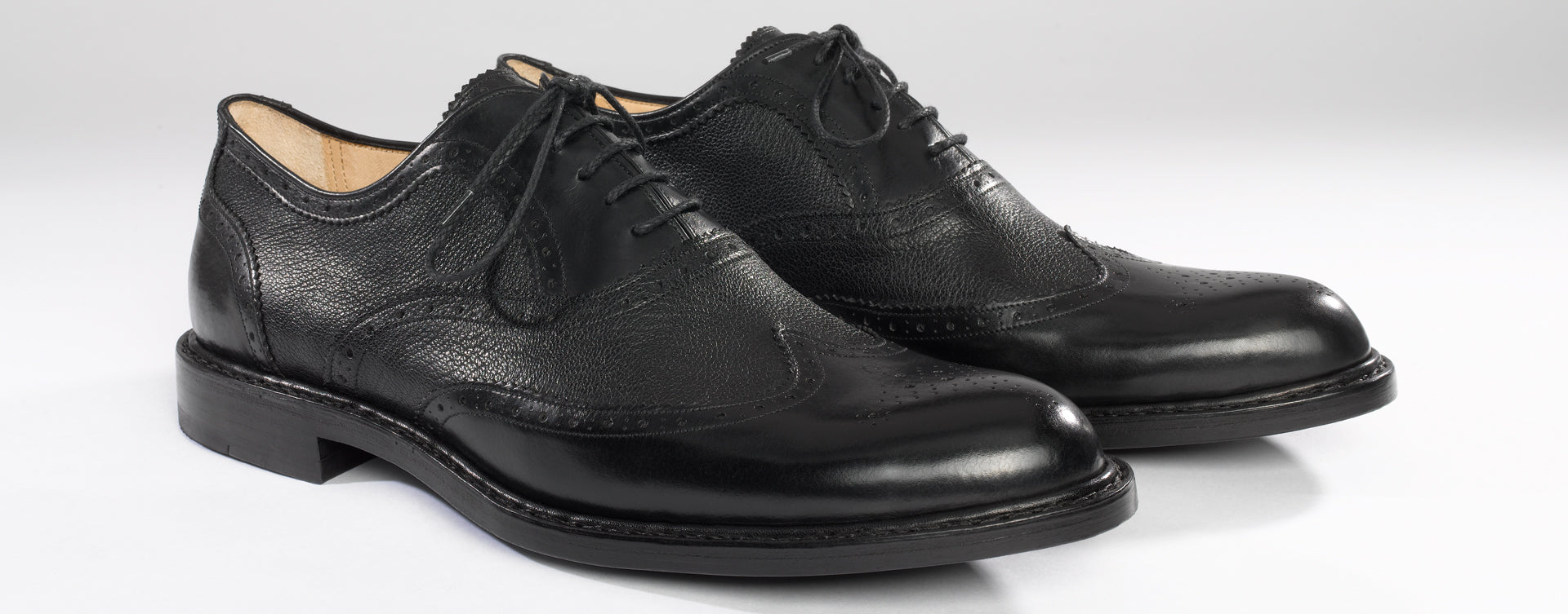 Maßgefertigter klassischer Herrenschuh Vitallo Brogue – schwarzes Boxcalf und Chevreau, schwarze Ledersohle – Paaransicht schräg von vorn